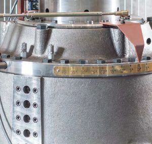 Detalle de carcasa metálica de gran equipo industrial con pernos, placa graduada en grados y puntero indicador, representando maquinaria marina de precisión