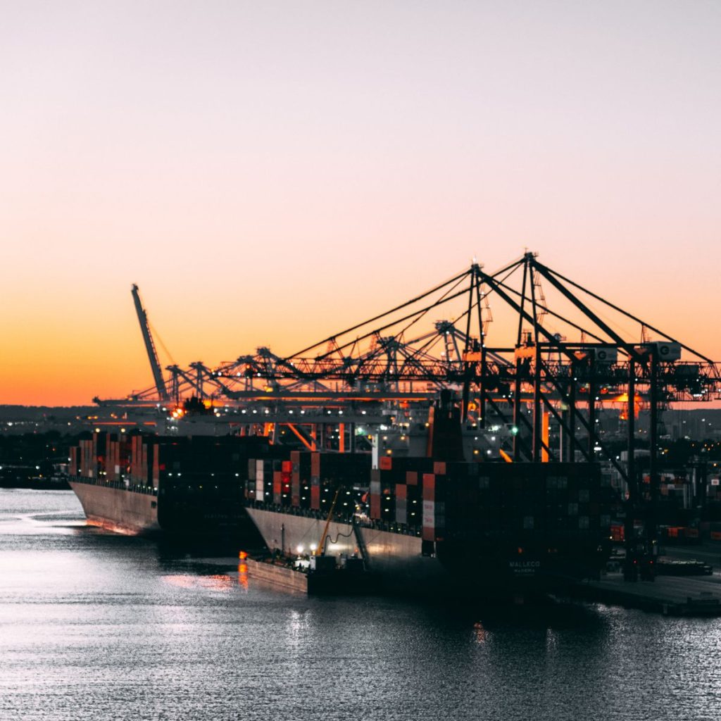 Buques portacontenedores atracados en terminal de carga con grúas pórtico al atardecer, vista del puerto marítimo iluminado sobre el agua